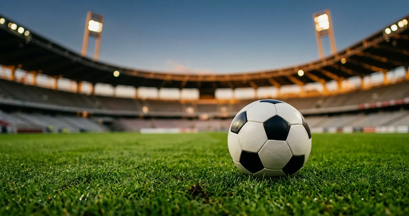 Ballon de football posé sur la pelouse d'un stade illuminé, banderoles floues en arrière-plan